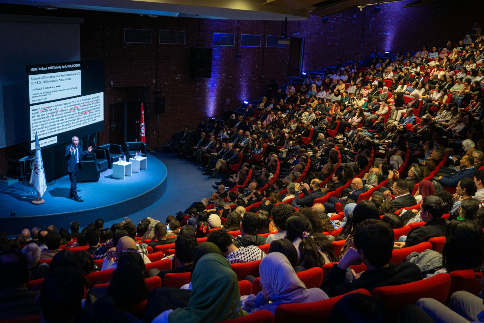 A speaker addressing a large audience in an auditorium